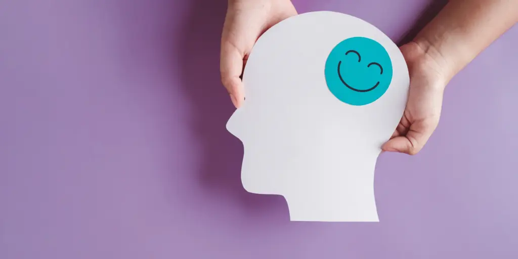 Hands holding a head-shaped cutout with a smiling face icon, symbolizing dopamine and its positive effects on the brain and mood.