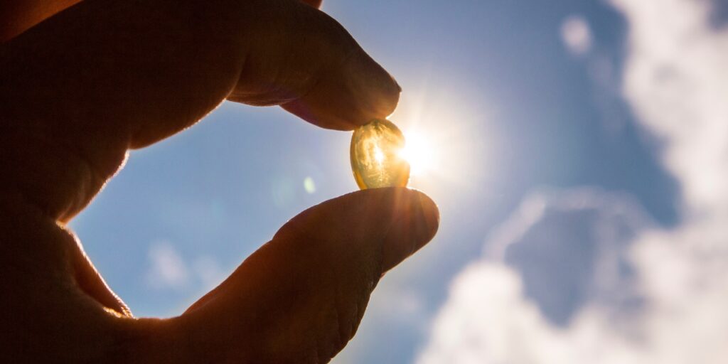 Vitamin d capsule is held between fingers against the sun