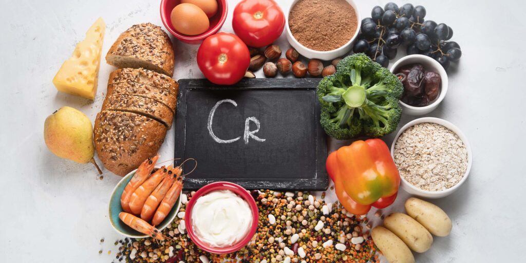 Selection of chromium-rich foods including broccoli, whole grains, eggs, shellfish, nuts, grapes, oats and potatoes arranged around a chalkboard displaying the chemical symbol Cr
