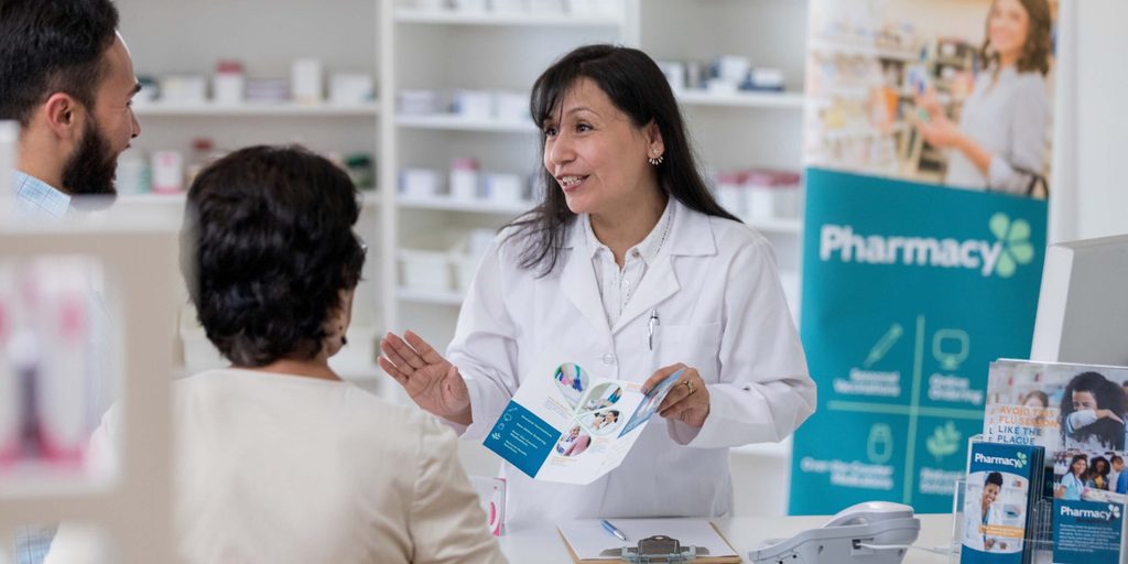 Pharmacist speaking with customers in a community pharmacy, highlighting the role of pharmacies in making dementia prevention and brain health support more accessible.